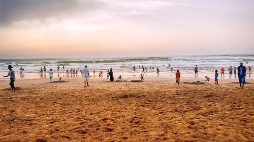 People enjoying on sand against sea during sunset