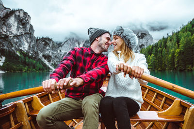 Rear view of couple sitting on lake against mountain