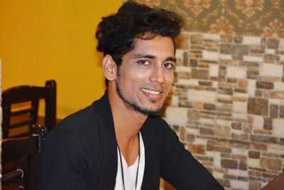 Portrait of smiling young man sitting against brick wall