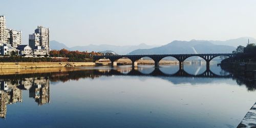 Bridge over river by buildings against sky