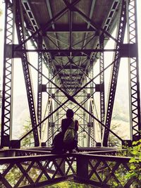 Rear view of man sitting under bridge