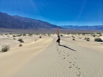 Full length of woman performing handstand on sand against blue sky at desert