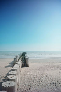 Wooden posts on beach against clear blue sky