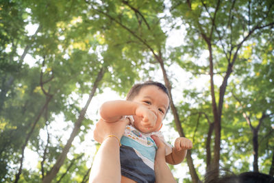 Low angle portrait of cute baby against trees