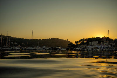 Sailboats moored at harbor against clear sky during sunset