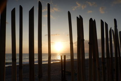 Silhouette wooden posts on beach against sky during sunset