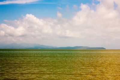 Scenic view of field by sea against sky