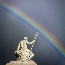 Statue on rainbow against sky