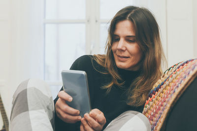 Relaxed girl using smartphone sitting on the sofa at home. woman chatting with friends on a couch 