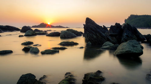 Rocks on sea against sky during sunset