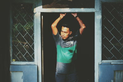 Portrait of young man standing against window