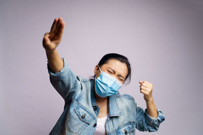 Young women wearing face mask with arms raised against wall