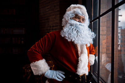Man wearing santa claus costume standing by window at home