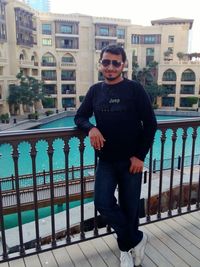 Portrait of young man standing by swimming pool against buildings