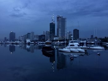 Sailboats in city against sky at dusk