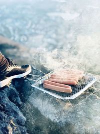 Low section of person by sausages over metal grate on rock