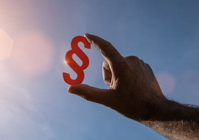 Low angle view of hand holding heart shape against sky