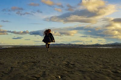 Rear view of girl running on beach against cloudy sky