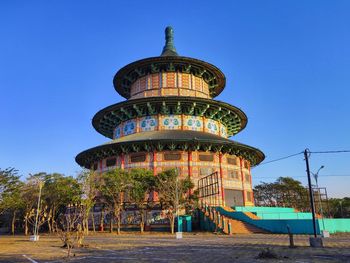 View of ferris wheel by building against blue sky