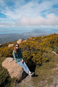 Portrait of smiling woman sitting on mountain against sky