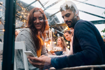 Low angle view of young man and woman using smart phone in glass cabin