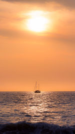 Silhouette sailboat in sea against orange sky