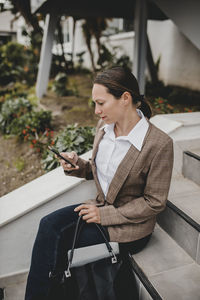 Woman looking at camera while sitting on mobile phone