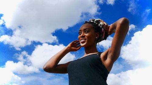 Low angle view of smiling young woman against sky
