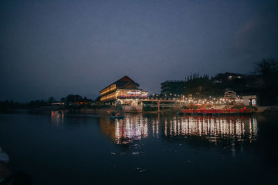 Illuminated buildings by lake against sky at night