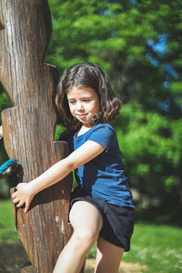 Caucasian beautiful girl hangs on a wooden pole from a rope swing in a park on a playground