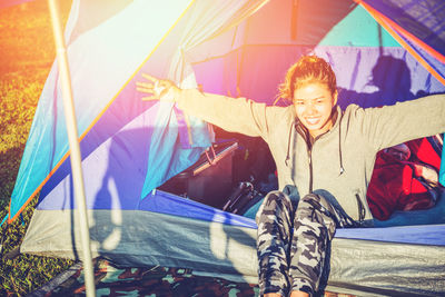 Portrait of smiling woman with arms outstretched sitting in tent