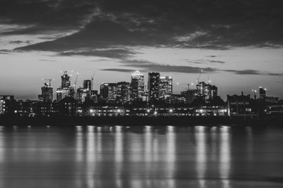 Illuminated city by river against sky