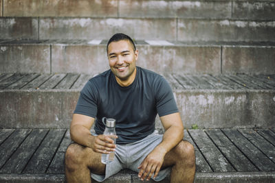 Portrait of smiling man holding water bottle while sitting on steps