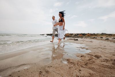 Full length of friends enjoying at beach against sky