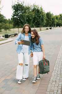 Two schoolgirls are holding a tablet in their hands and watching a video, laughing on the way 