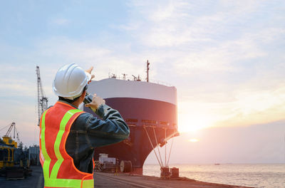 Man working by sea against sky during sunset