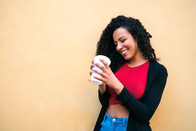Smiling young woman holding ice cream standing against wall