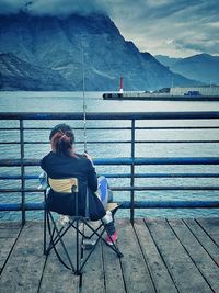 Rear view of woman sitting on railing against sea