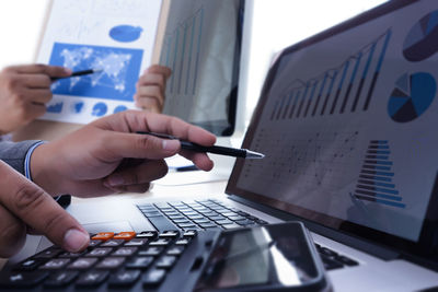 Cropped hands of businessman analyzing data over laptop and calculator on desk in office