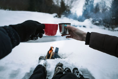 Low section of people toasting tea cups while sitting on snow covered field