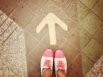 Low section of woman standing by arrow sign on footpath