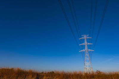 Low angle view of electricity pylon on field against clear blue sky