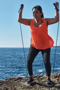 Fitness woman in sports set training with elastic band,weights gym exercises, in front of the water	