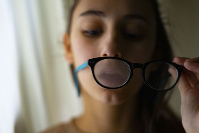 Young woman blowing and cleaning her glasses.