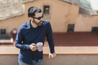 Relaxing moment of a middle-aged man standing on the balcony drinking coffee