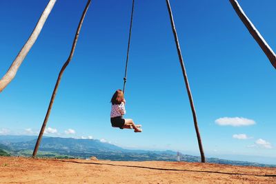 Rear view of girl on swing against sky