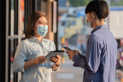 Colleagues wearing mask looking at digital tablet while standing outdoors