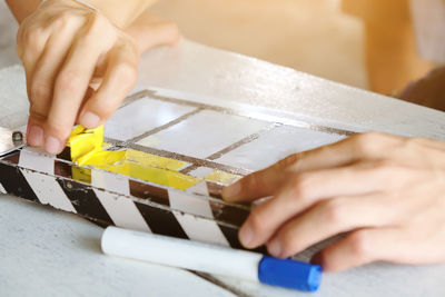 Close-up of cropped hands removing yellow tape from film slate