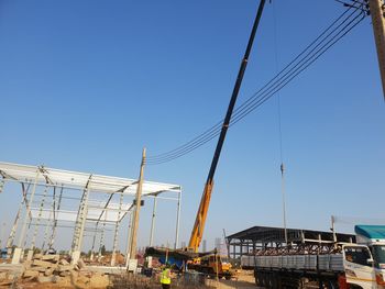 Low angle view of cranes against clear blue sky