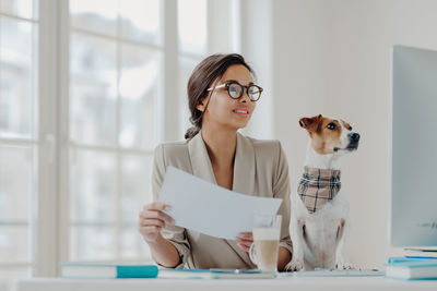 Smiling young woman with dog using computer on desk in office